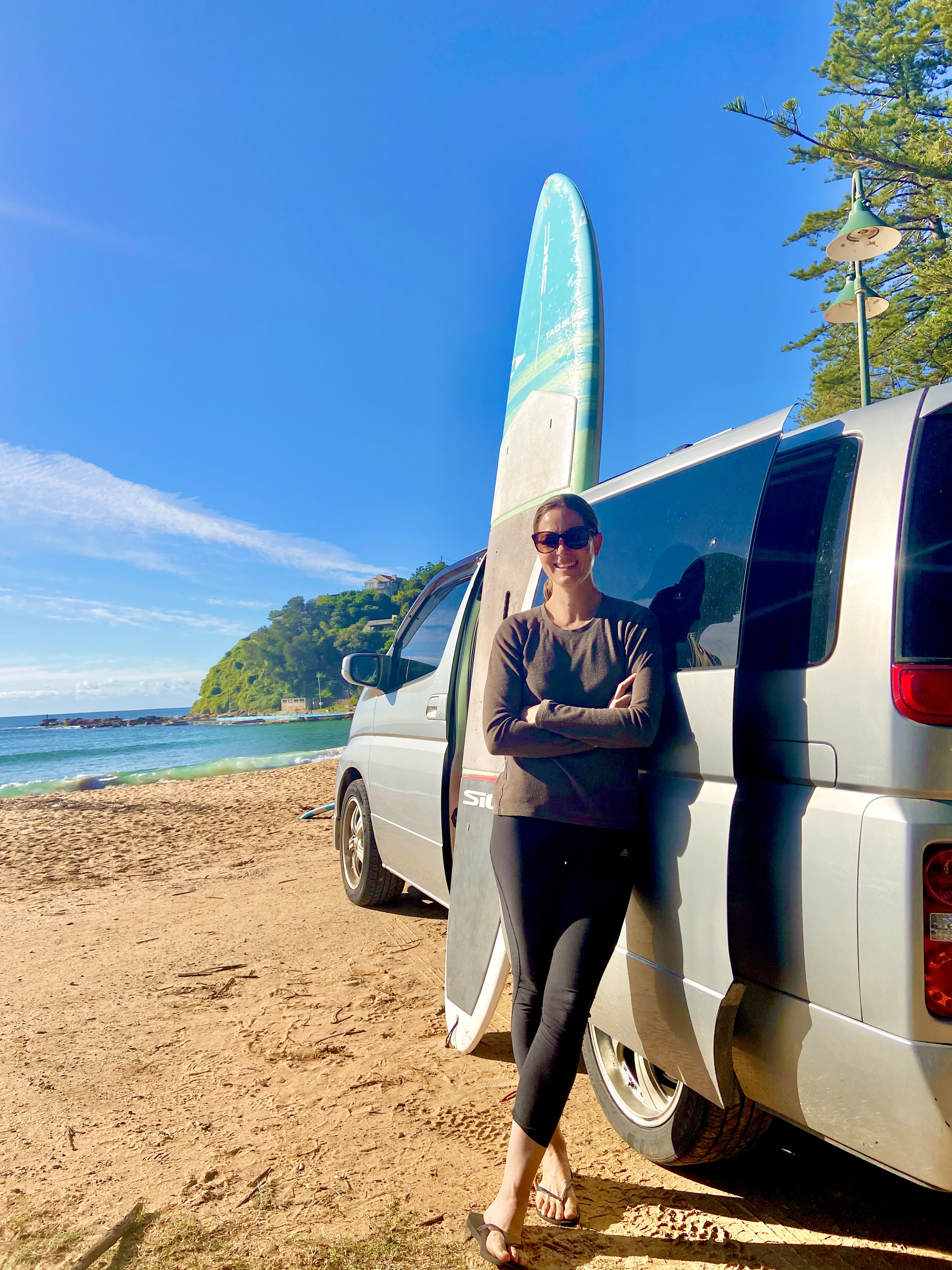 Vanarchy owner Annabelle Hender standing next to campervan and paddleboard on Palm Beach
